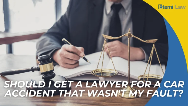 Gavel and scales on desk with person writing, introducing question about hiring a lawyer after a car accident